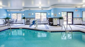 Une piscine intérieure avec un sol carrelé en bleu et blanc, un escalier d’accès à la piscine et un espace détente avec des chaises et des tables.