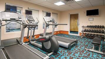 A gym with treadmills, a stationary bike, and a weight bench. There are dumbbells on a rack and a television on the wall.