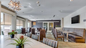 A modern hotel lobby with a long dining table, comfortable seating, and a large TV screen. - Residence Inn by Marriott Clearwater Downtown (Clearwater)