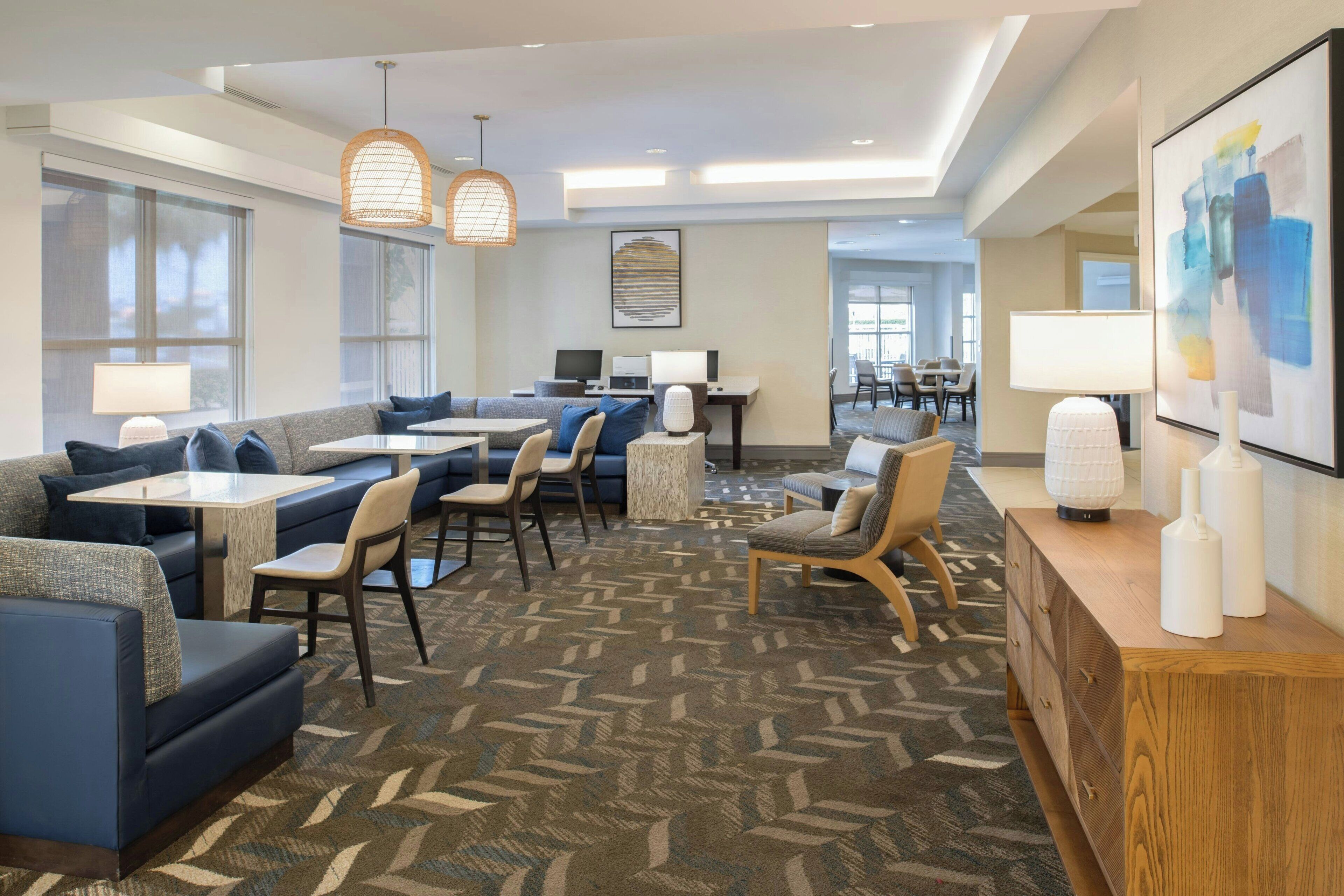 A modern hotel lobby with seating areas, a reception desk, and large windows.