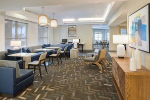 Eine moderne Hotelhalle mit Sitzbereichen, einer Rezeption und großen Fenstern.
