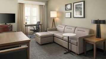 A hotel room with a sectional sofa, a desk, a television, and a lamp.