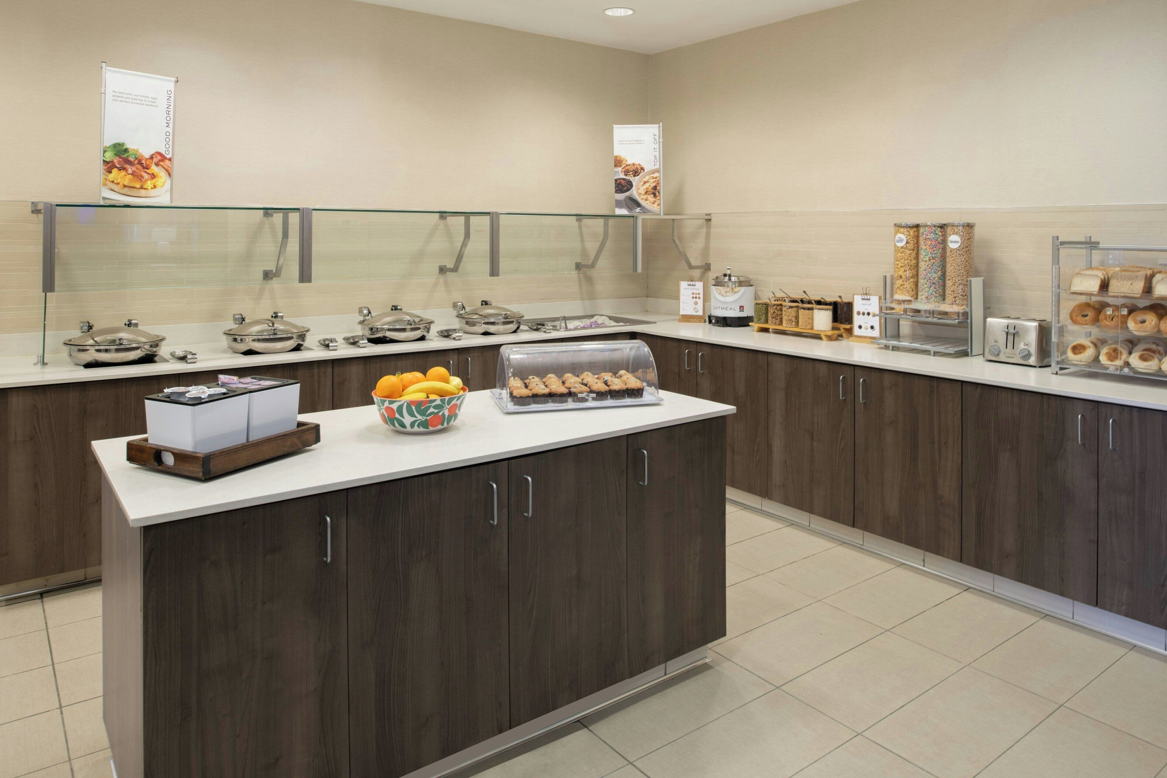 A modern breakfast bar with a variety of food items, including fruits and pastries, and a coffee machine.