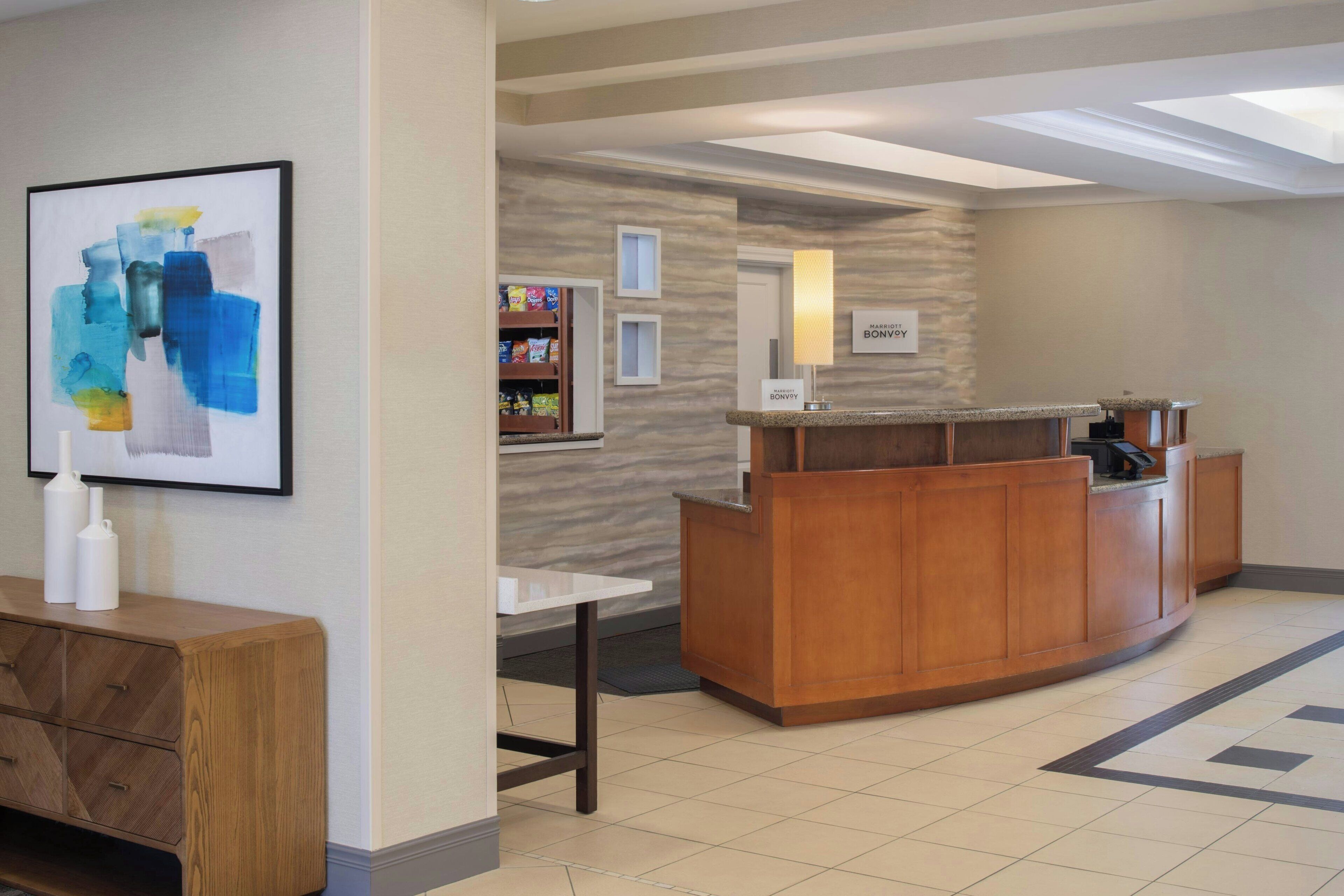 A reception area with a wooden reception desk, a framed abstract painting, a small table, and a wall-mounted sign.