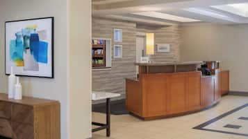 A reception area with a wooden reception desk, a framed abstract painting, a small table, and a wall-mounted sign.