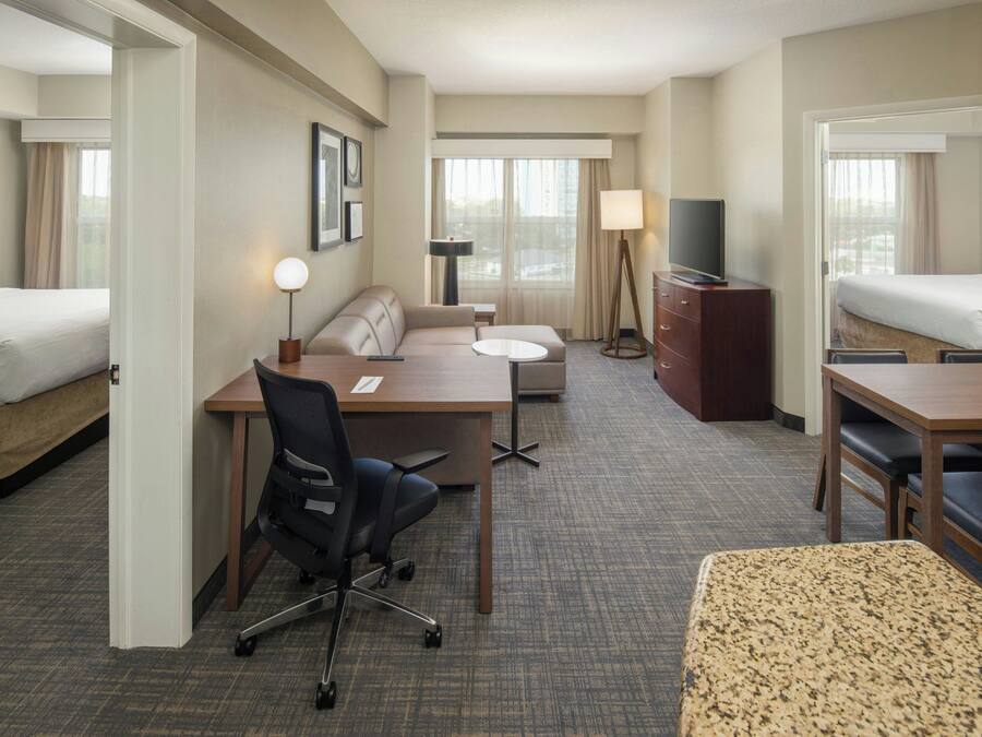 A hotel room with a bed, a desk with a chair, a sofa, a small table, a TV, and a dresser.
