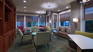 A modern hotel room with a dining area, seating with patterned chairs, a sofa, and a large window offering a view of the outside. - Residence Inn Bryan College Station (College Station)