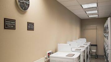 A laundry facility with multiple washing machines, a clock, and signs indicating cycle times and available supplies.