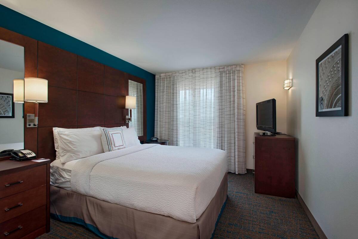 A hotel room with a large bed, a desk with a telephone, a television on a stand, and a mirror on the wall.