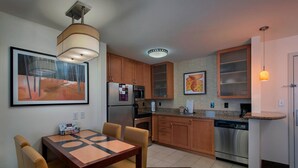 A compact kitchen with wooden cabinets, a stainless steel refrigerator, a dishwasher, and a dining area with a table and chairs. - Residence Inn Bryan College Station (College Station)