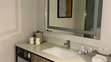 A modern bathroom with a large mirror, two sinks, and a wooden vanity.