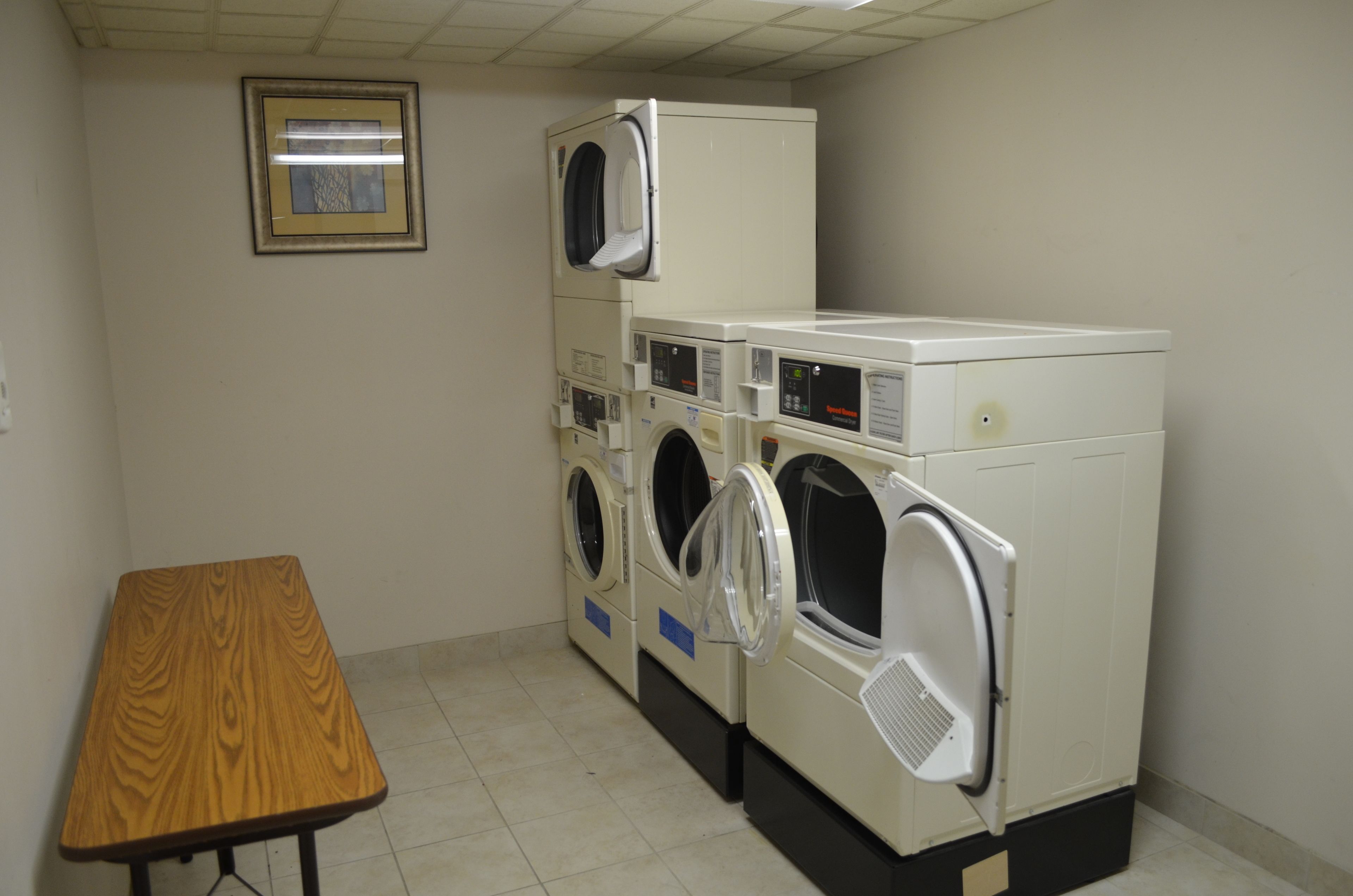 A laundry room with multiple washing machines, a wooden table, and a framed picture on the wall.