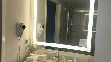 Un bany amb un mirall gran, un lavabo, un assecador i una dutxa que es veu al reflex.