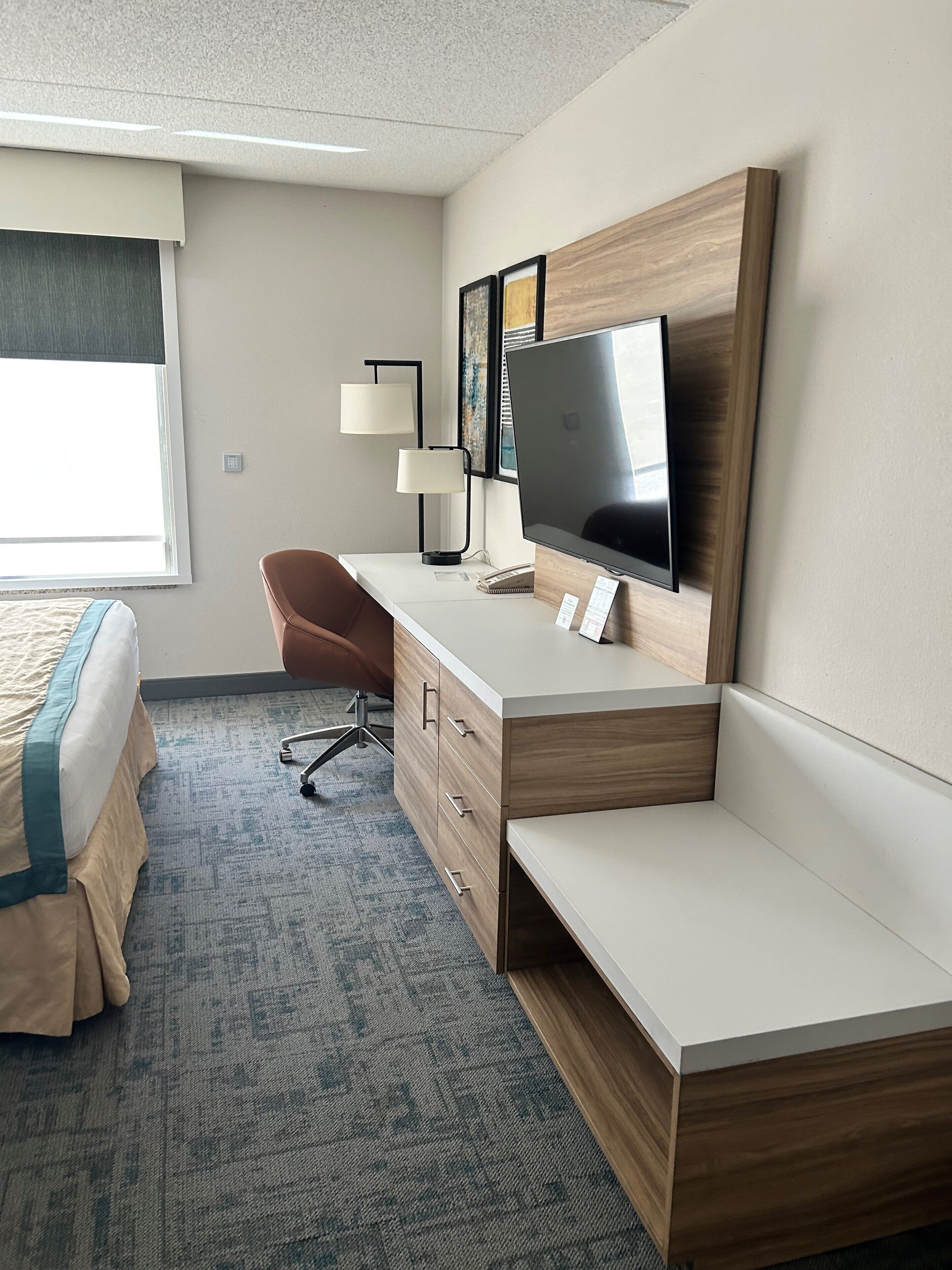 A hotel room with a bed, a desk with a computer, a TV, and a chair.