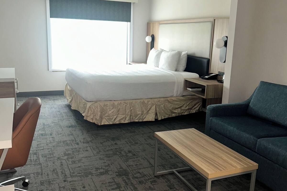 Ein Hotelzimmer mit Bett, Schreibtisch, Stuhl, Sofa und einem kleinen Tisch.