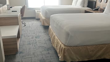 A hotel room with two beds, a desk, a chair, a lamp, and a window.