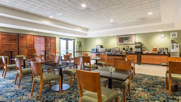 Un comedor de hotel con mesas y sillas, una cocina al fondo y una alfombra estampada.