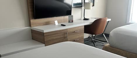 A hotel room with a large bed, a desk with a flat-screen TV, a chair, and artwork on the wall.
