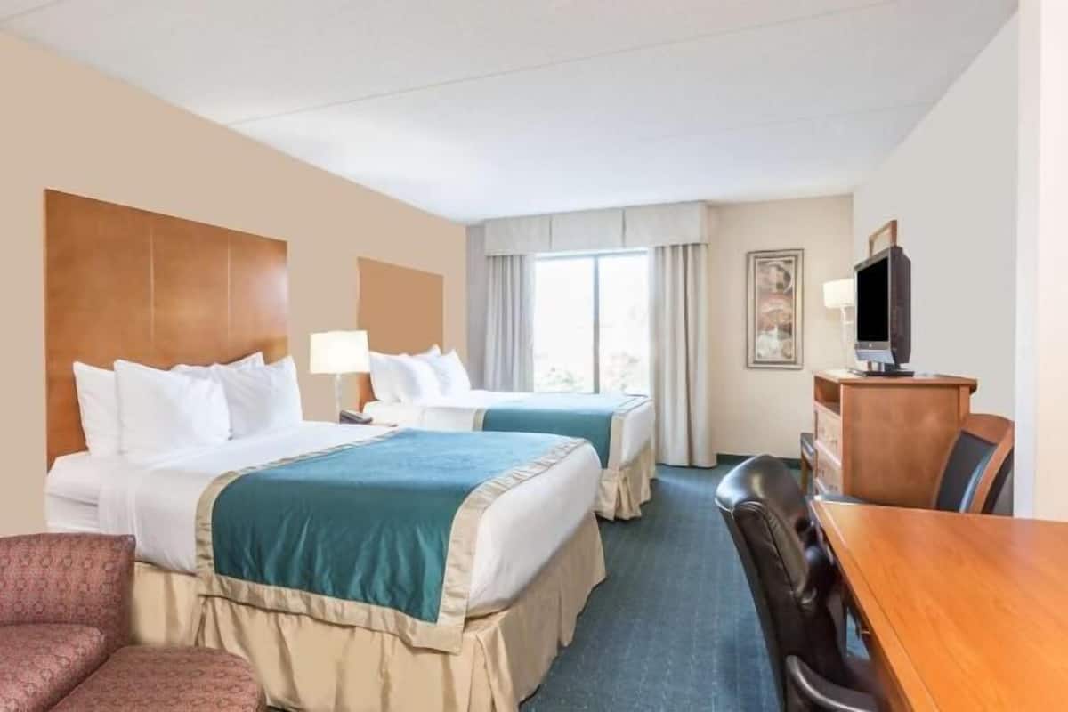 Ein Hotelzimmer mit zwei Betten, einem Schreibtisch, einem Fernseher und einem Sessel.