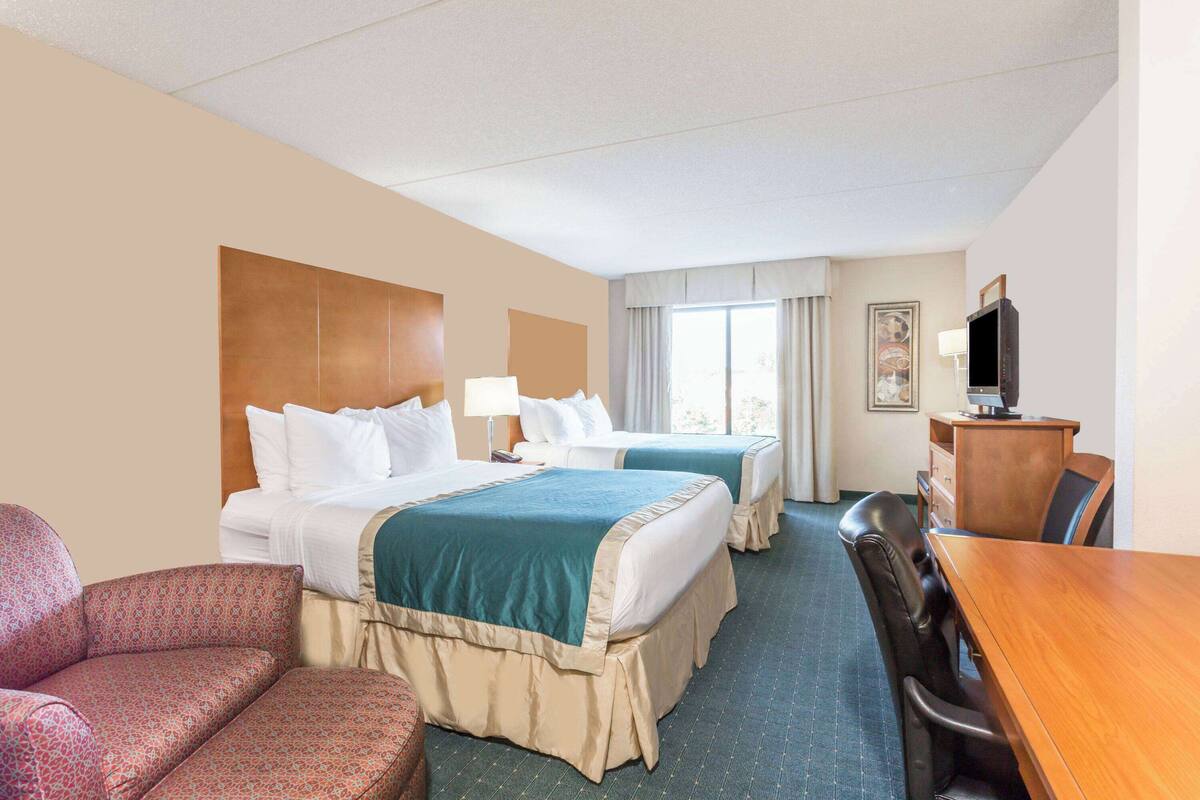 Ein Hotelzimmer mit zwei Betten, einem Schreibtisch, einem Sessel und einem Fernseher.
