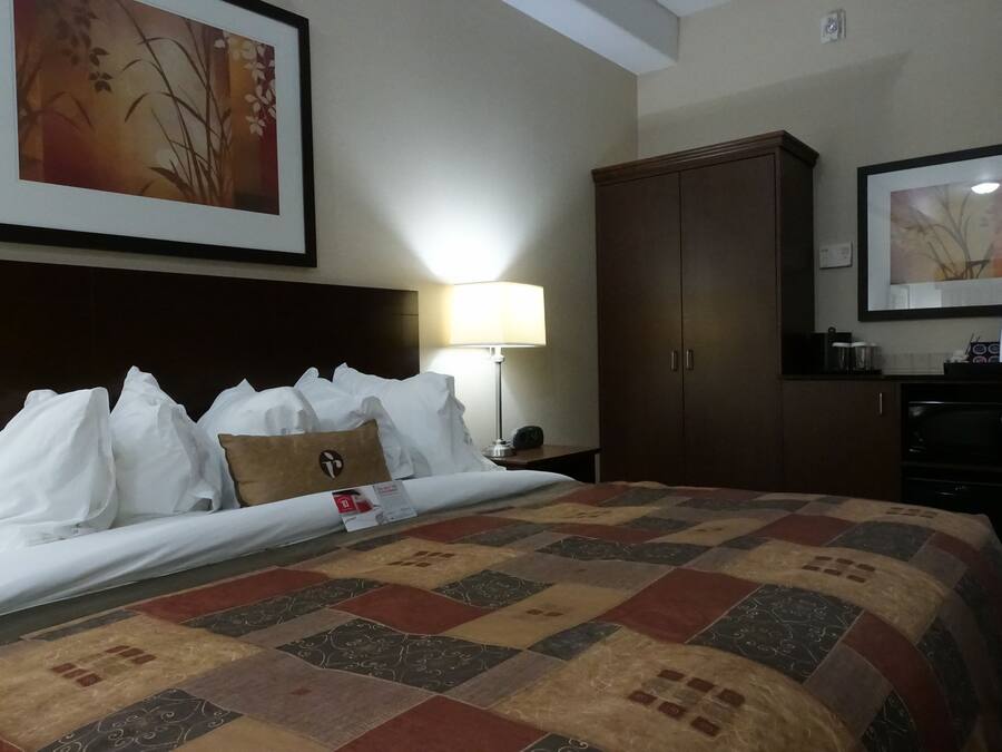A hotel room with a large bed, a wooden wardrobe, a nightstand with a lamp, and a framed picture on the wall.
