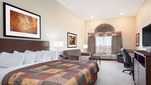 Una habitación de hotel con una cama grande, un escritorio, una silla, un televisor y una ventana con cortinas.