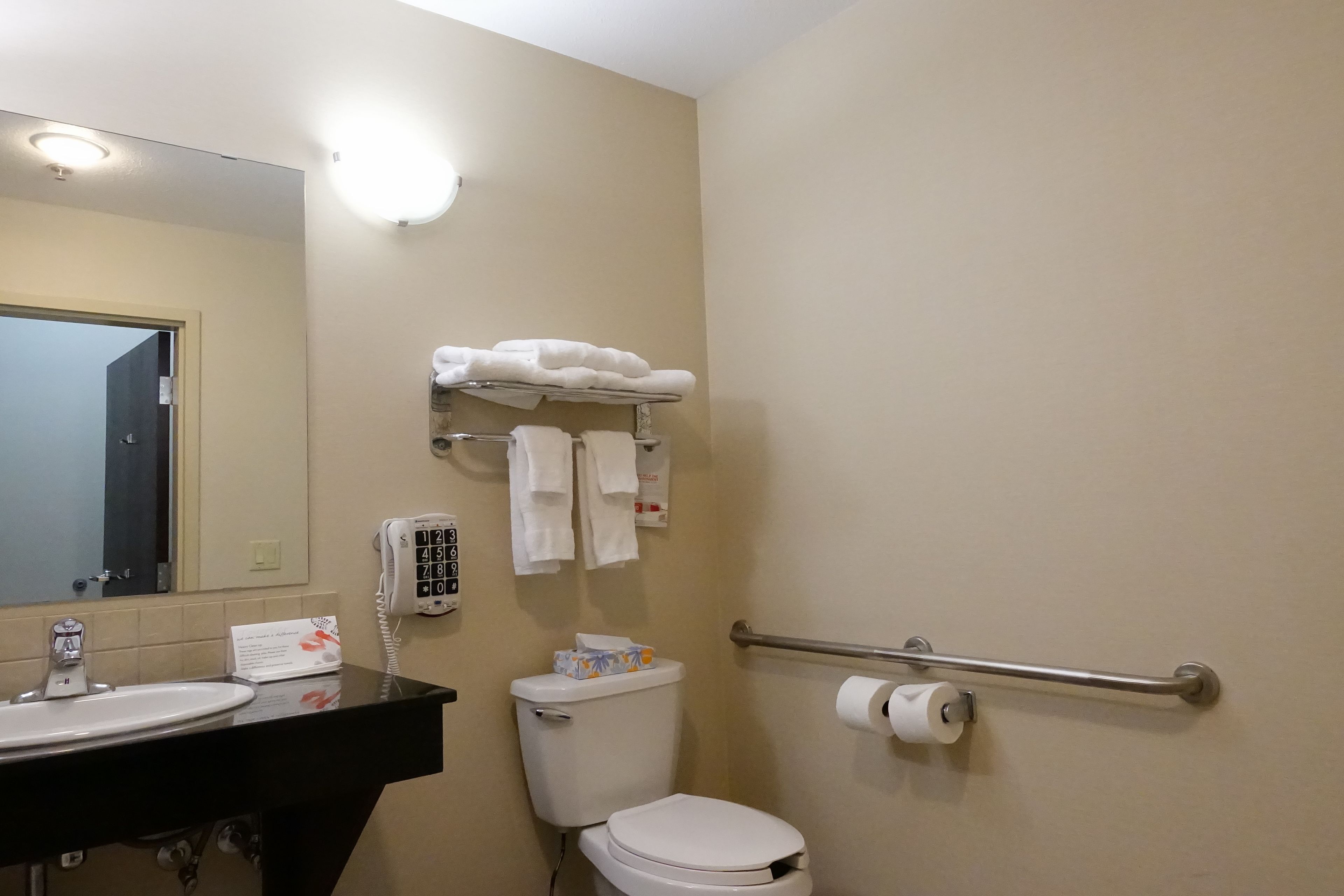 A bathroom with a sink, toilet, and hand dryer. There are towels and a phone on the wall.