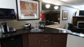Una cocina moderna con lavavajillas integrado, cafetera y lavabo. Hay un florero con flores rojas en la encimera.