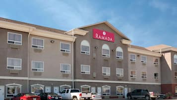 Un hôtel Ramada à la façade marron, doté de nombreuses fenêtres et d’un parking où sont garées plusieurs voitures.