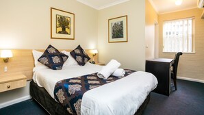 A hotel room with a bed, bedside tables, a desk, and a chair. There are two framed artworks on the walls.