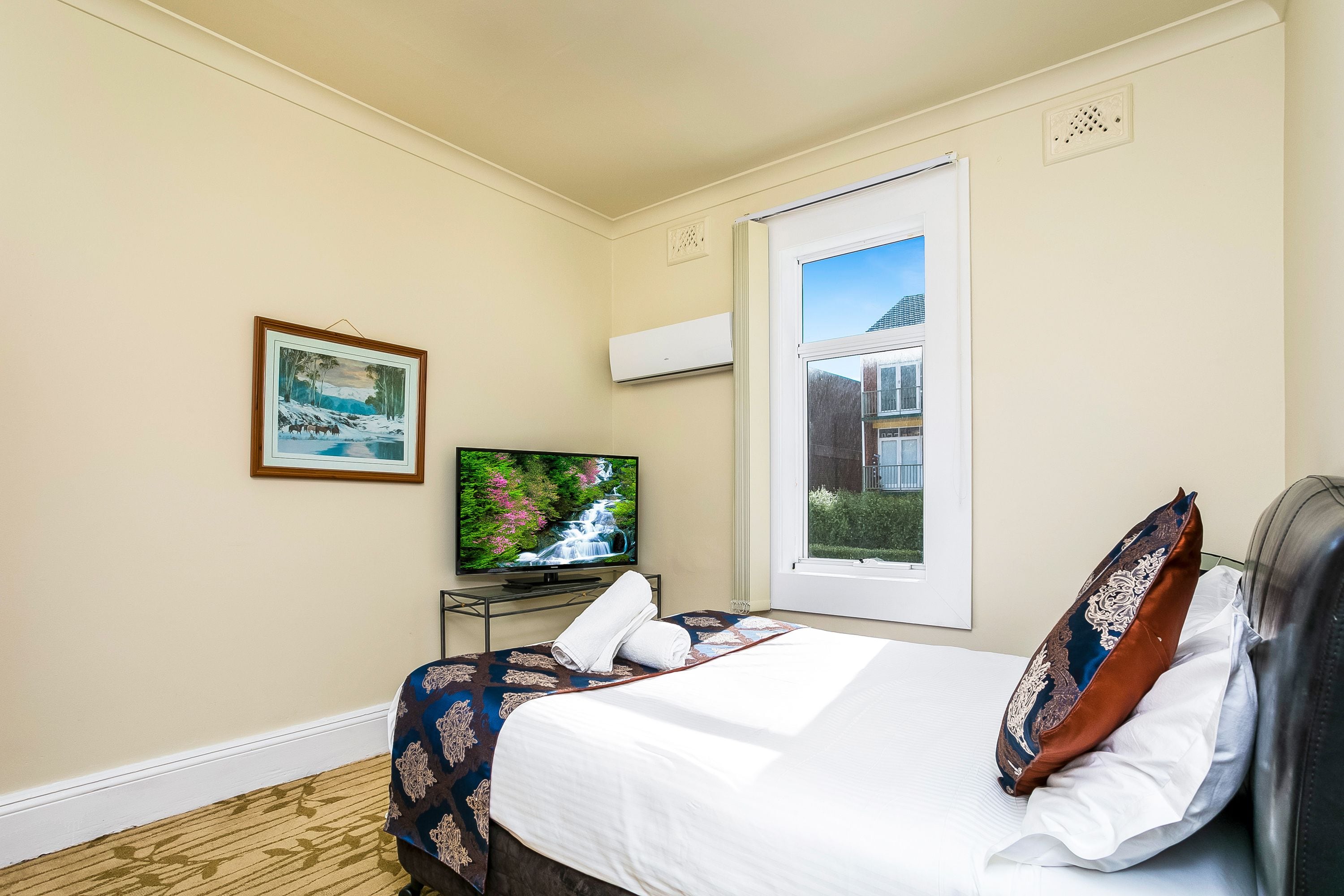 Una habitación de hotel con una cama, televisión, ventana y un cuadro en la pared.