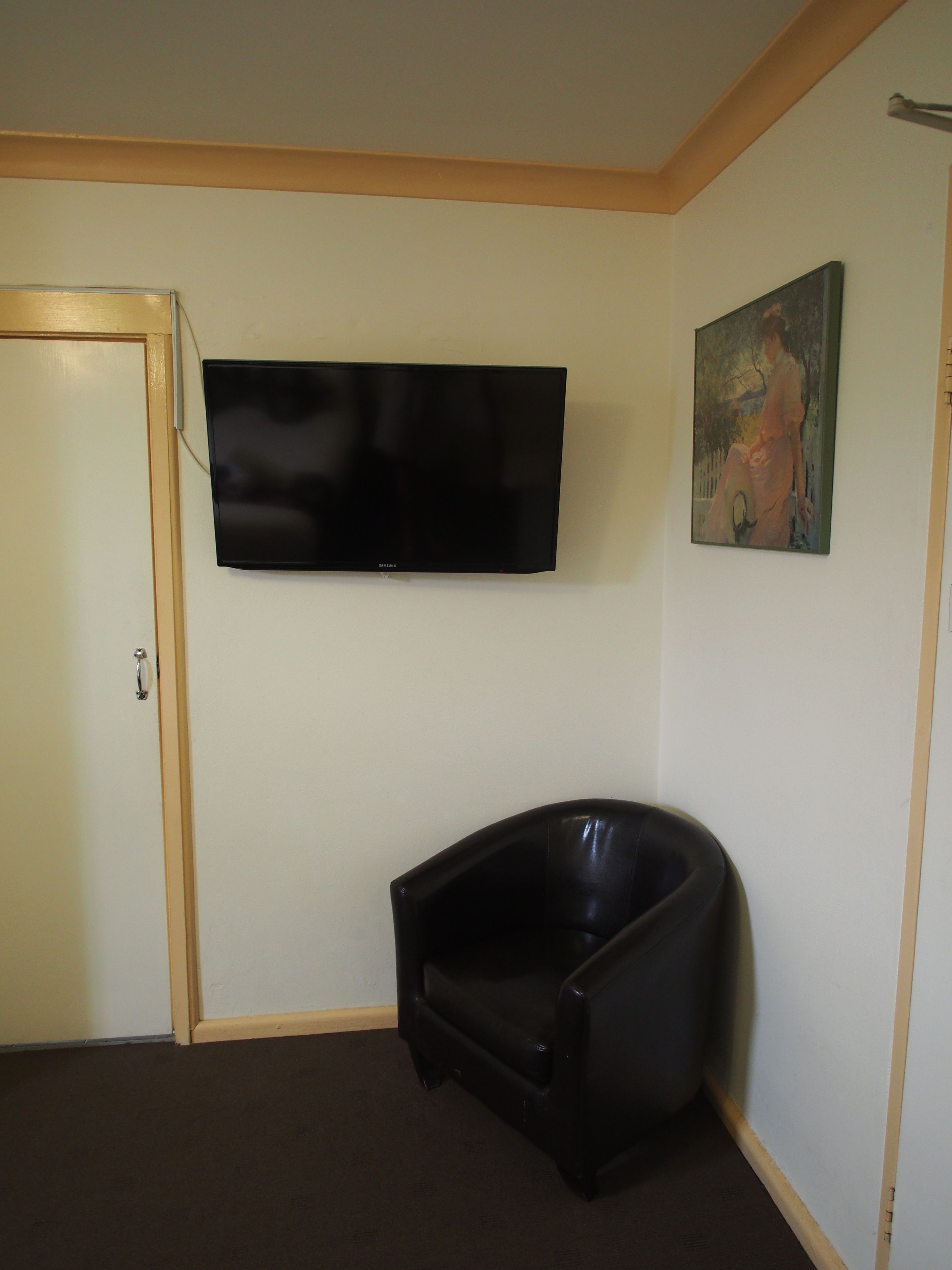 A room with a flat-screen TV mounted on the wall, a black leather chair, and a door with a wooden frame.