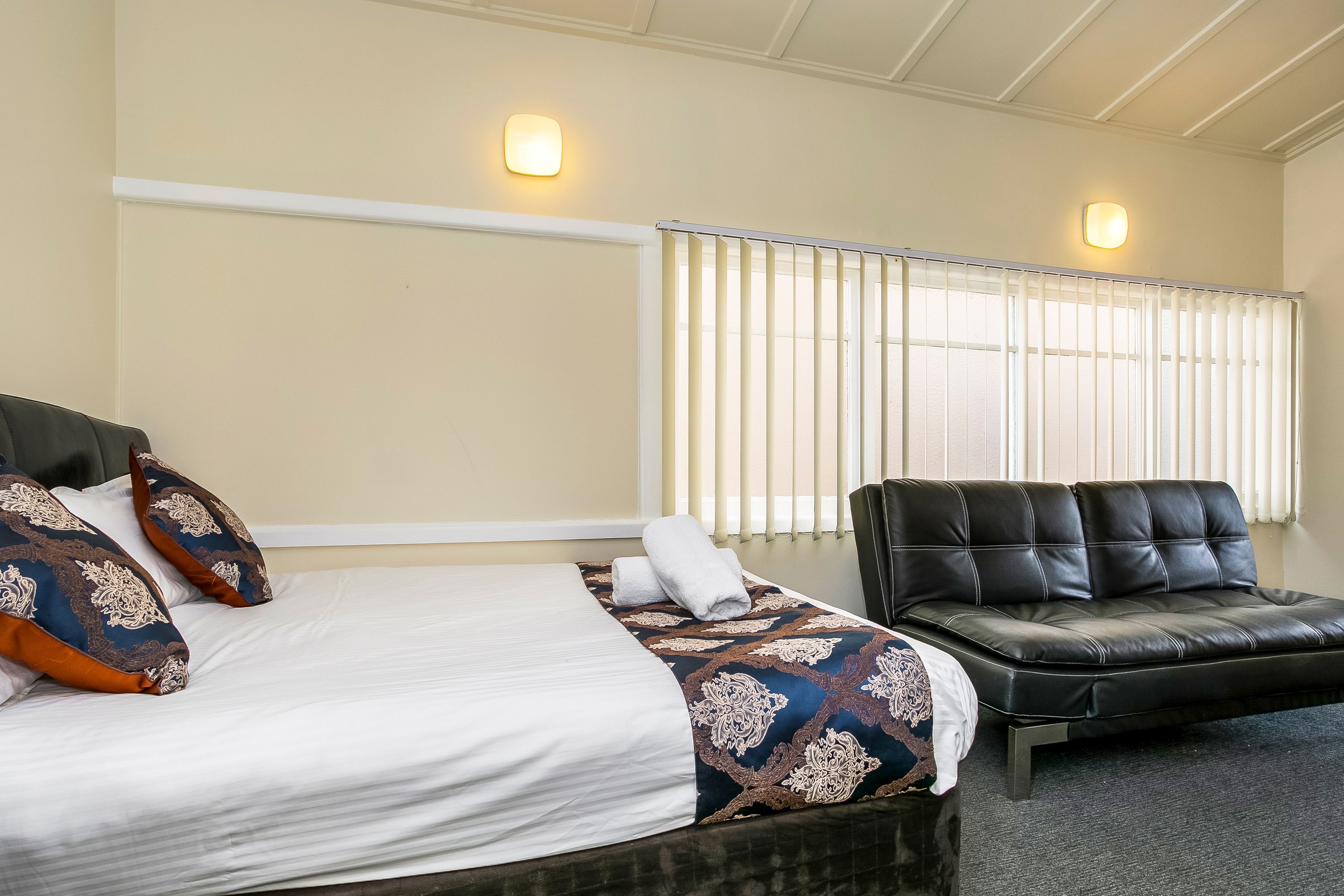 A hotel room with a bed, a black leather sofa, and two wall-mounted lights.