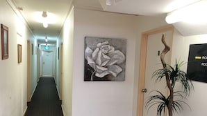 A hallway with a carpeted floor, a painting of a flower on the wall, and a potted plant.