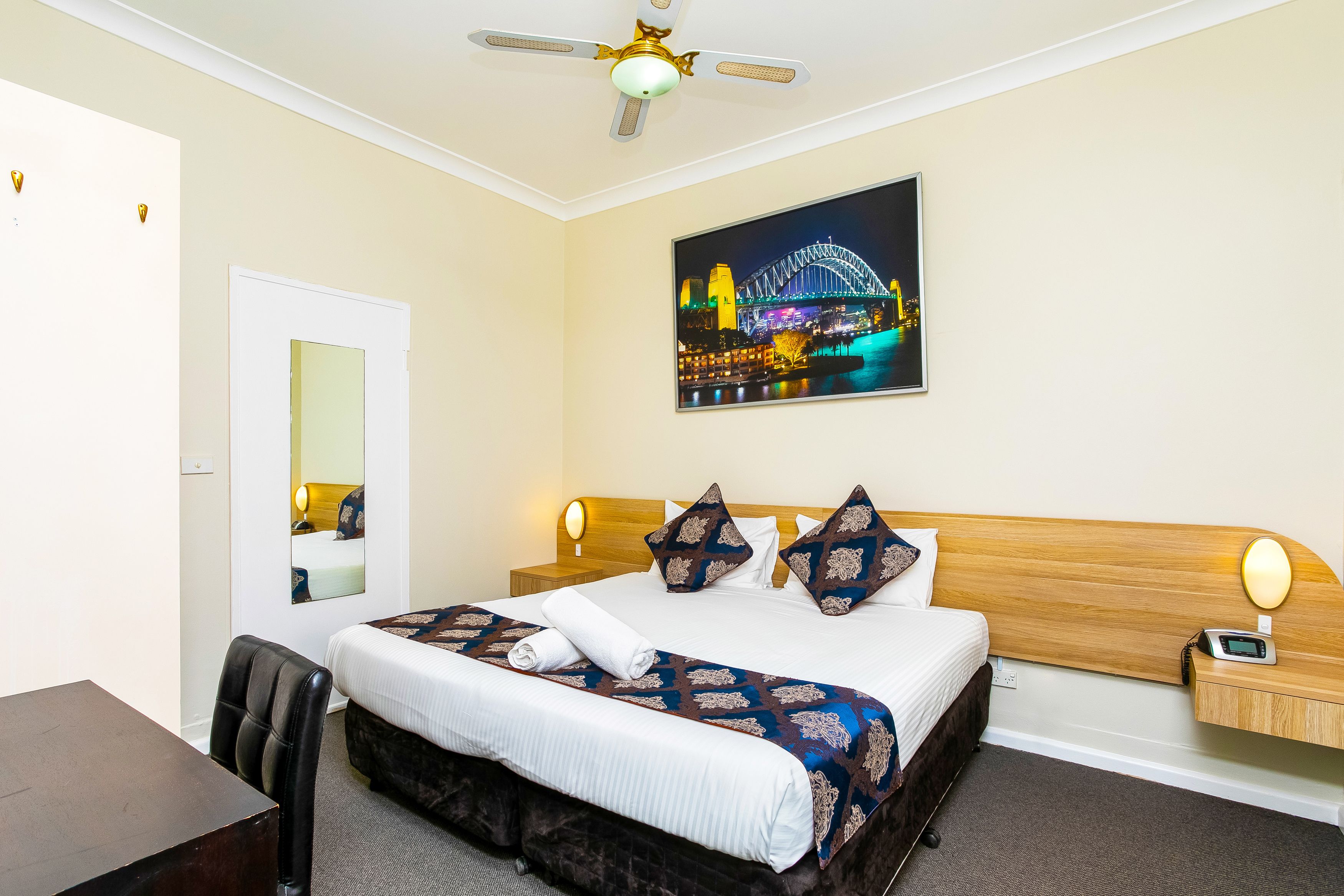 A hotel room with a bed, bedside table, chair, and a ceiling fan.