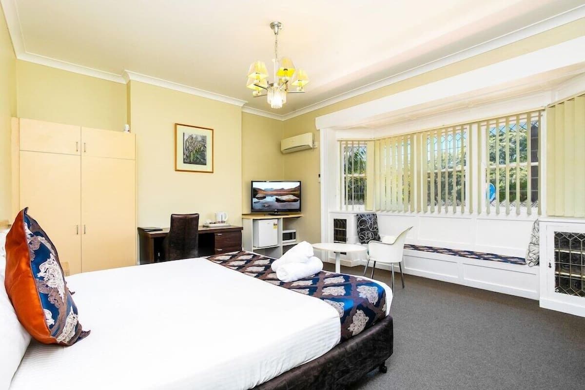 A hotel room with a bed, a desk, a television, and a window seat.