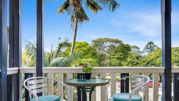 A balcony with two chairs and a table, overlooking a lush green landscape and a clear blue sky.
