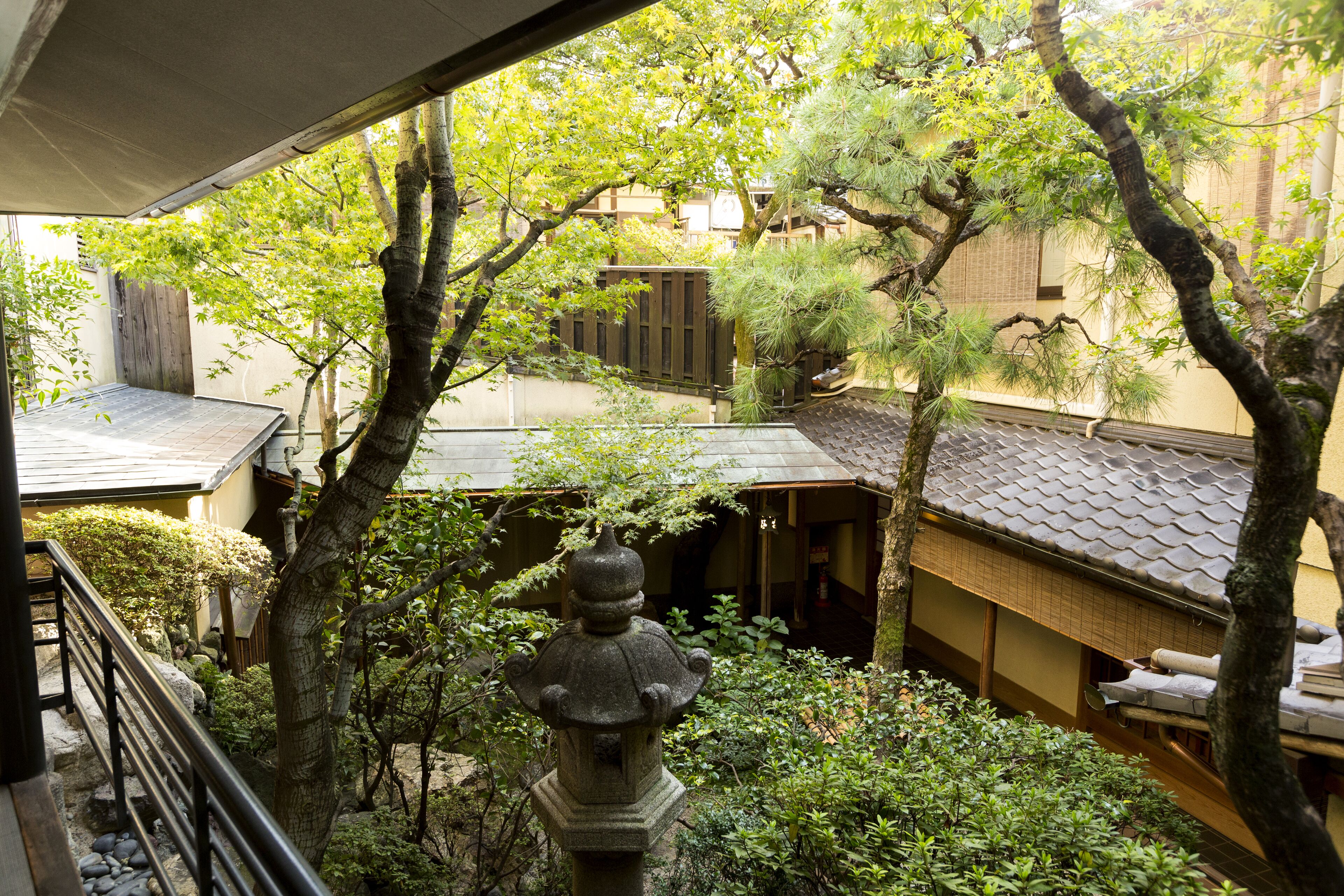 A traditional Japanese garden with a stone lantern, bamboo, and a view of a residential area with tiled roofs.