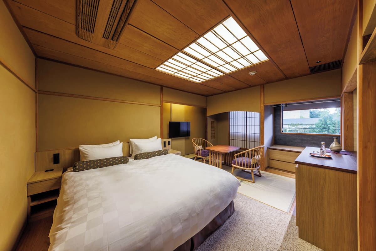 A hotel room with a large bed, a desk, a chair, a TV, and a window with a view.