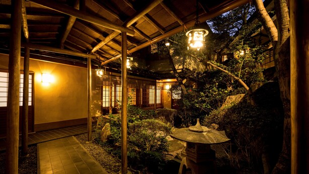 A traditional Japanese garden with a stone lantern, wooden walkway, and bamboo structures.
