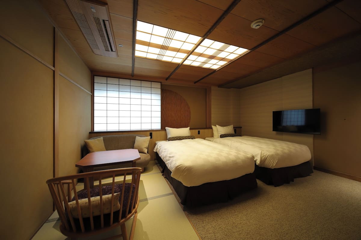 A hotel room with a large bed, a small table, a chair, and a TV mounted on the wall.