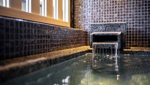 A small, rectangular water feature with a stone base, situated in a corner with tiled walls and a wooden frame.