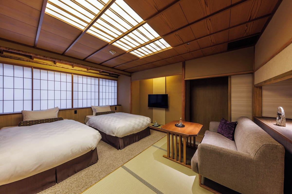 A traditional Japanese-style room with tatami flooring, two beds, a sofa, a small table, and a TV.