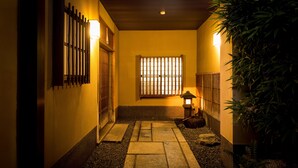 A hallway with a tiled floor, a wooden door, a window with vertical bars, and a lantern.