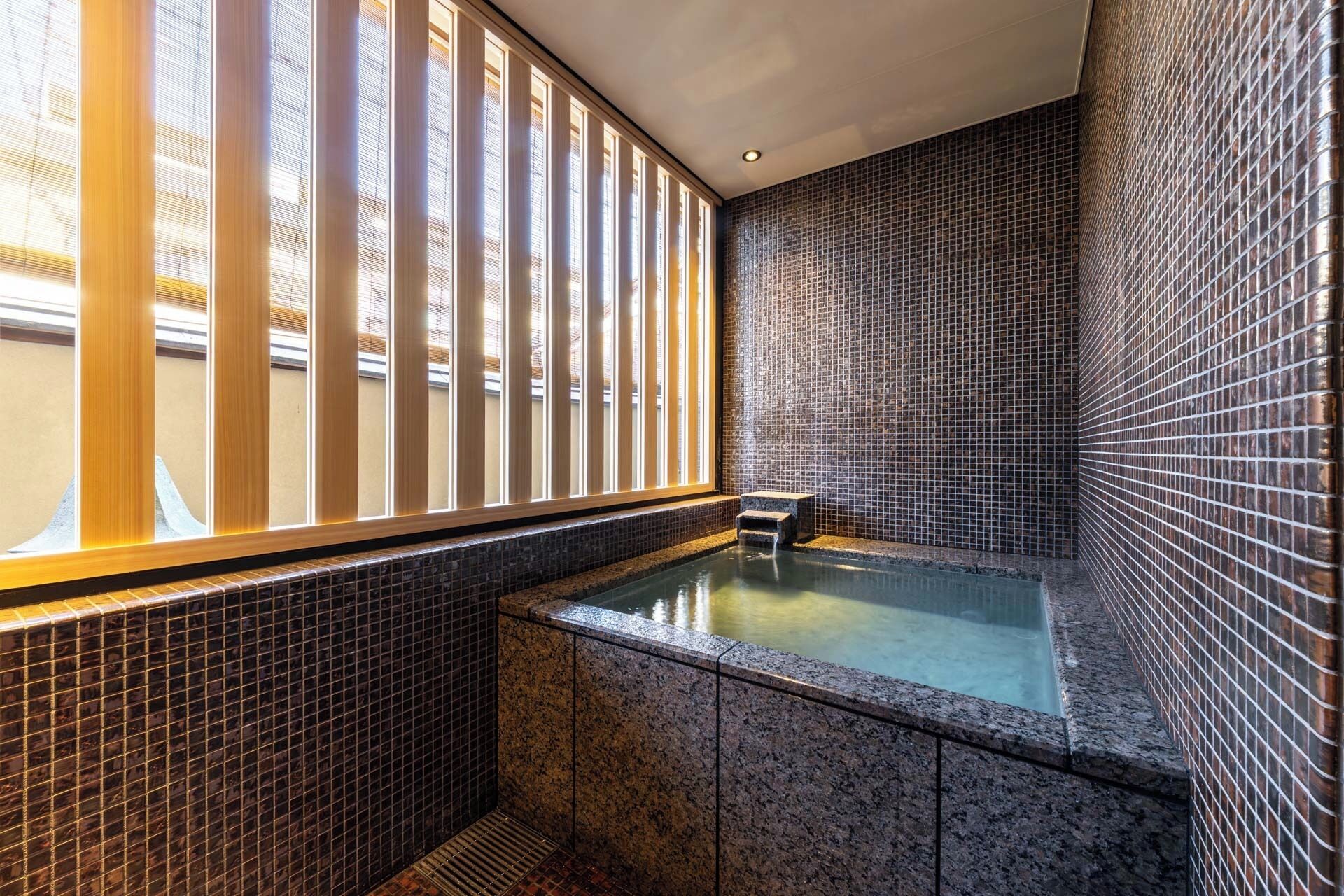 A spa area with a hot tub, tiled walls, and a window with vertical blinds.