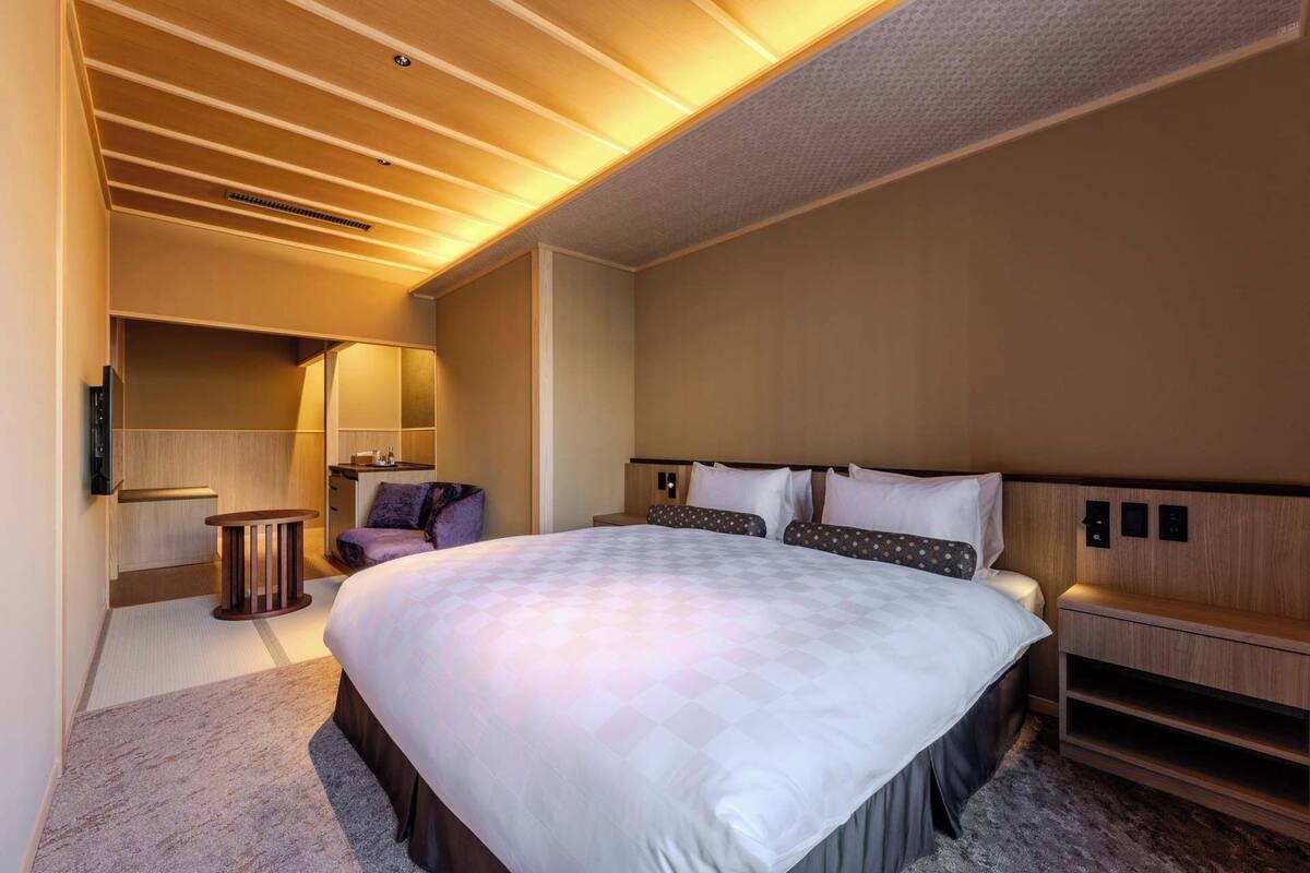A modern hotel room with a large bed, a desk, a chair, and a small table.