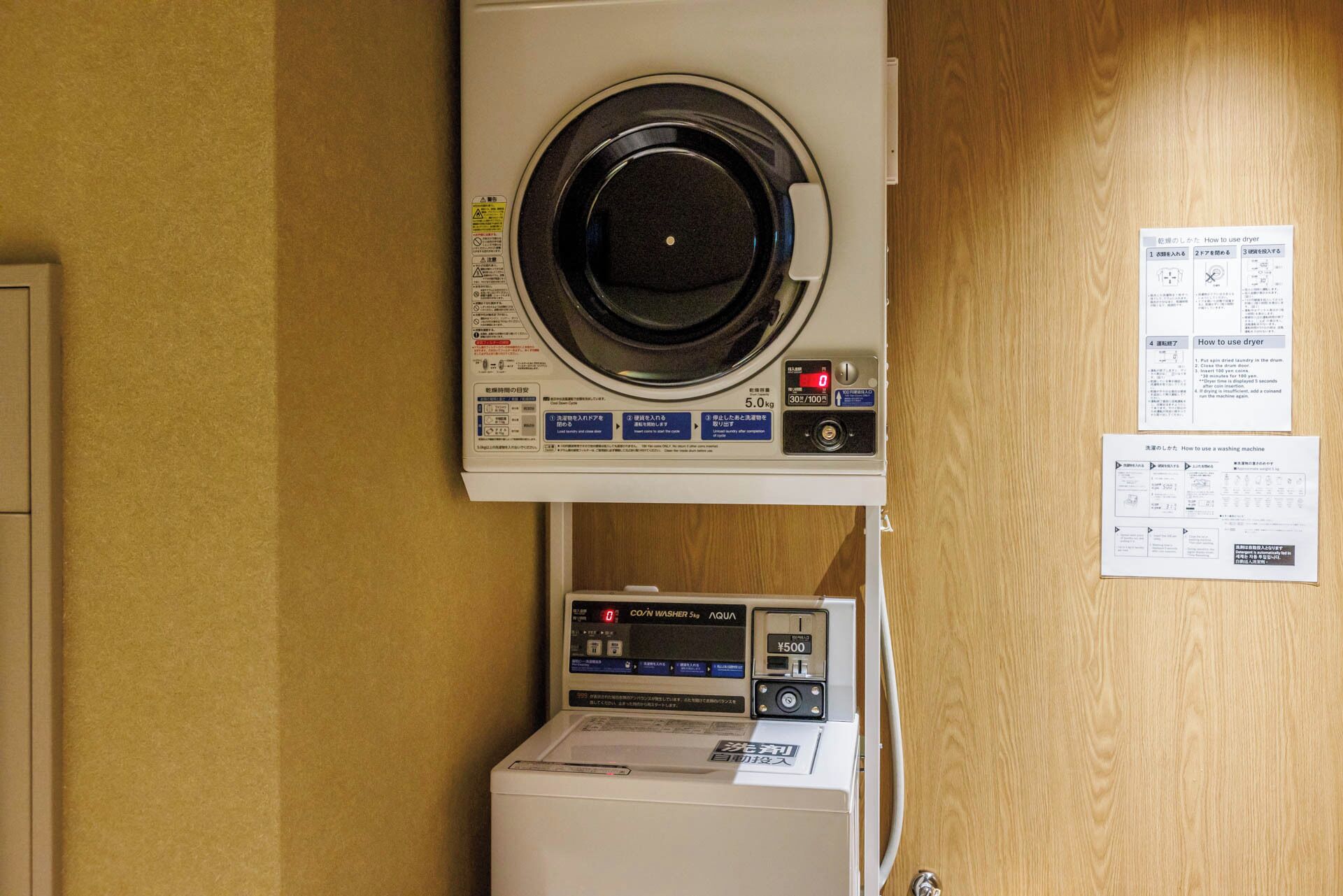Eine Waschmaschine mit Frontlader, darunter ein Trockner und an der Wand befestigte Gebrauchsanweisungen.