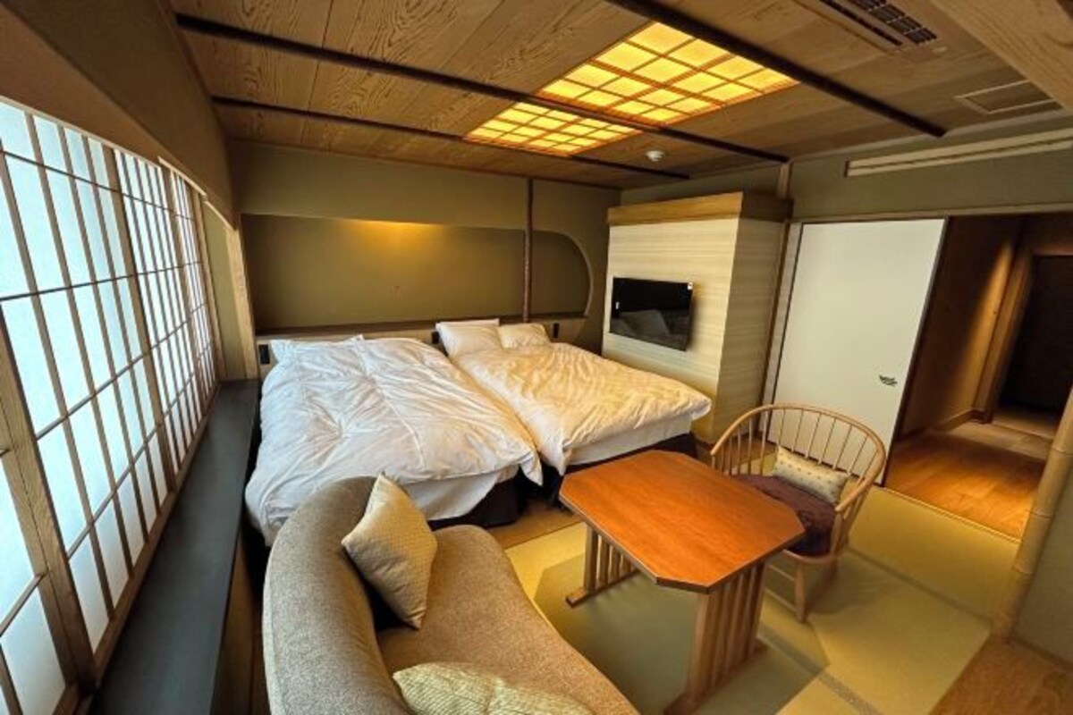 Ett litet rum med en säng, en soffa, ett litet bord och en tv som är monterad på väggen.
