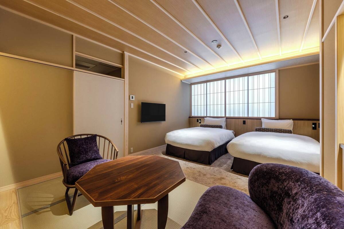 A hotel room with a wooden ceiling, two beds, a TV, and a small table.
