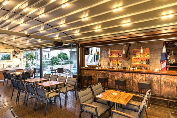 A bar area with a stone wall, wooden tables, and chairs, and a view of the outdoors. - Elotis Suites (Chania)